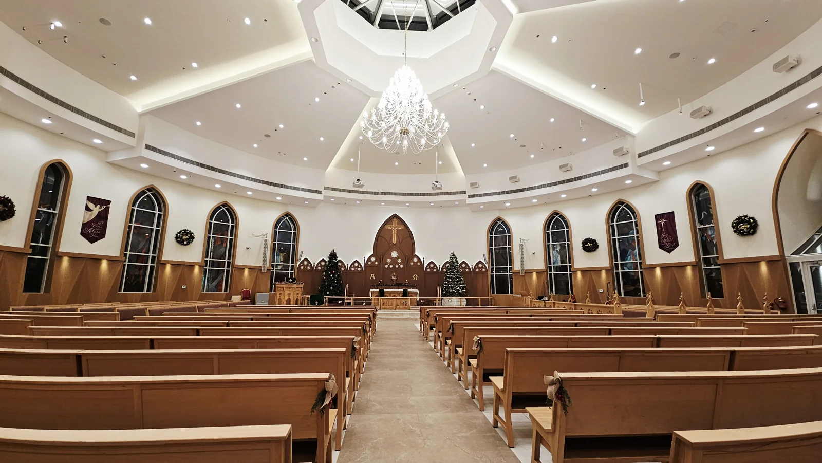 A wide view of the sanctuary, showing the full rows of wooden pews, central aisle and chandelier